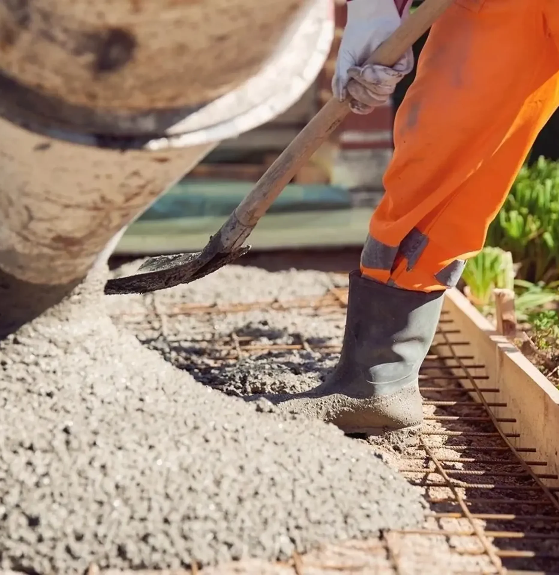 Worker pouring and spreading wet concrete.